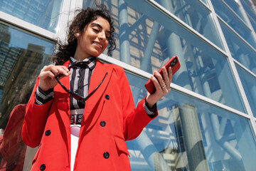 Cheerful manager browsing cellphone near glass wall