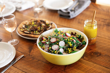 A garden salad in a yellow bowl on a rustic wooden table.