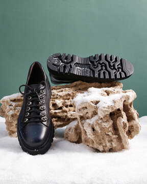 Men's winter shoes stand on a stone in the snow.