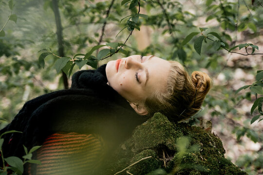 Blonde Woman With Closed Eyes Lying On Rock In Forest