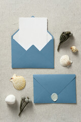 Wedding stationery set in nautical style. Wedding invitation card, blue envelopes, seashells, flowers on pastel beige background. Flat lay, top view, copy space.