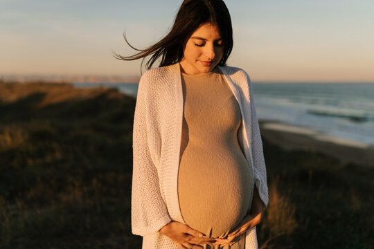 Calm pregnant woman hugging belly on seaside