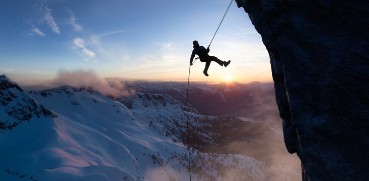 Adult adventurous man rappelling down a rocky cliff. Extreme adventure composite. 3d rendering mountain artwork. Aerial background landscape from British Columbia, Canada. Sunset Sky