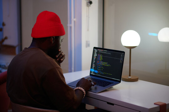 black man with a hat coding on his laptop 