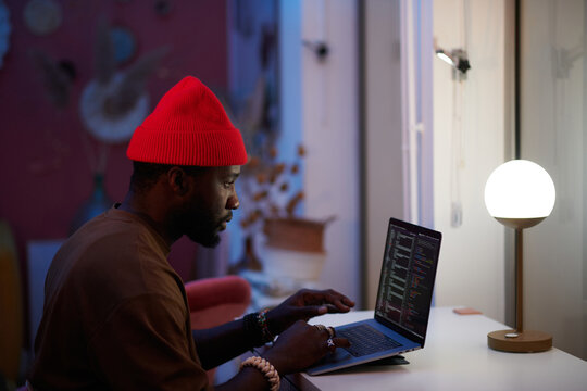 man with hat coding on his laptop