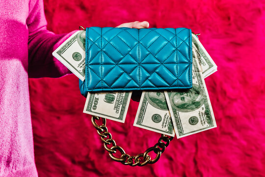 holds a blue purse full of fake dollar bills