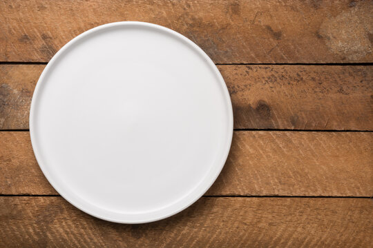 empty white plate on a wooden table top, food photography background or backdrop, horizontal top view with copy space 