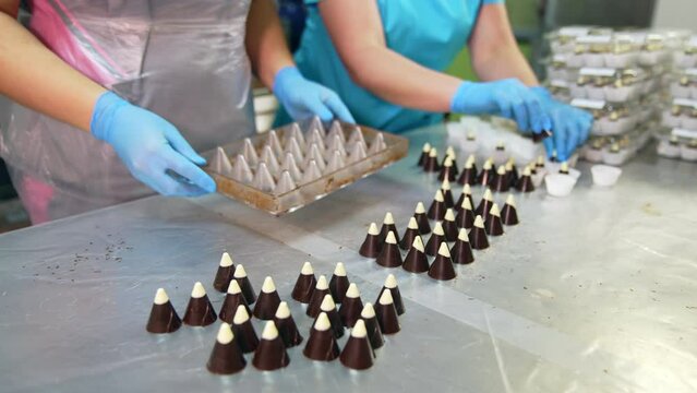 Confectionery worker extracts candies from molds. Other worker puts ready-made sweets into a packaging paper. Close up.