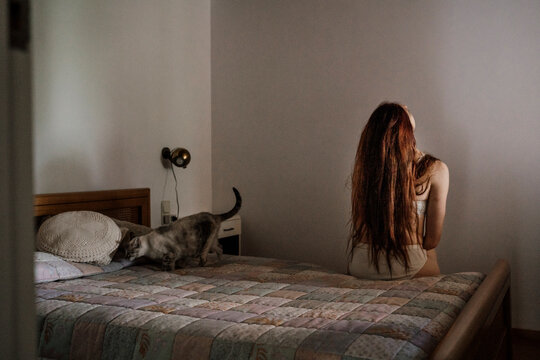Back view of woman sitting on bed with cat