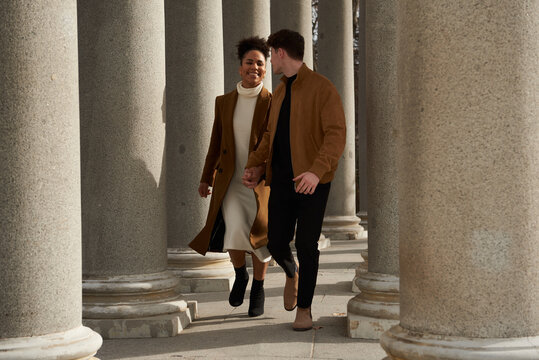 Couple running while holding hands between columns