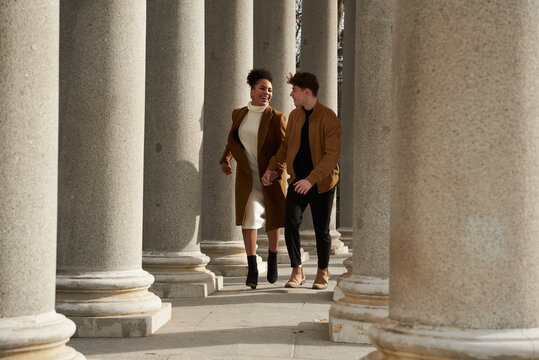 Couple running while holding hands between columns