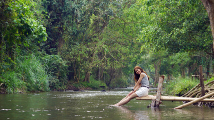 Happy young asian woman sitting near the stream, smiling and looking to the camera in the forest, enjoy traveling on holidays.