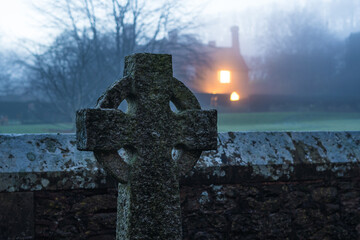 A Celtic cross gravestone with a house in the distance