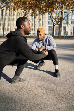 Athlete doing squats with trainer on sports ground