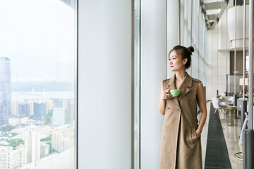 asian woman standing by window looking at view