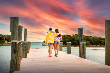 Two friends walking along a ocean pier together watching a beautiful picturesque sunset while on vacation