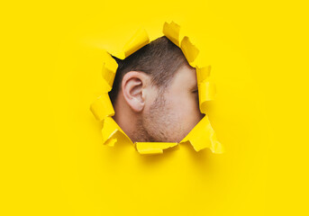 A man's ear is visible through a torn hole in the yellow paper. The concept of eavesdropping,...