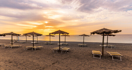  empty beach during beautiful sunrise or sunset with chaise loungues and nice umbrellas with blue sea, sun glow and amazing cloudy sky on thr background