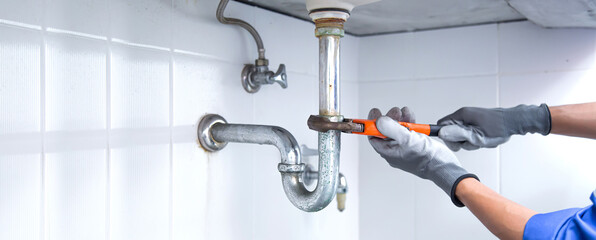 Technician plumber using a wrench to repair a water pipe under the sink. Concept of maintenance, fix water plumbing leaks, replace the kitchen sink drain, cleaning clogged pipes is dirty or rusty. - obrazy, fototapety, plakaty