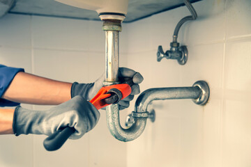 Technician plumber using a wrench to repair a water pipe under the sink. Concept of maintenance, fix water plumbing leaks, replace the kitchen sink drain, cleaning clogged pipes is dirty or rusty.