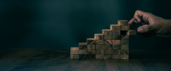Close-up hand pulls wood block tower stacked in pyramid stair step with caution to prevent collapse...