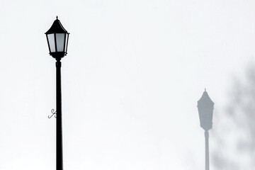 A black street lamp against a white wall. Beautiful retro-style lantern. Shadows on the wall. Black and white