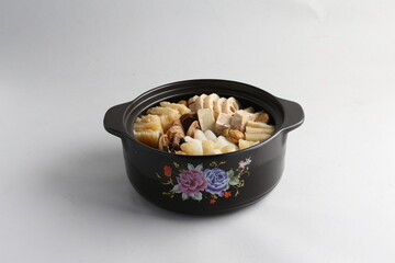freshly hot stewed Peng cai with  seafood and meat in herbal sauce clay pot and yellow cover on white background Chinese traditional menu