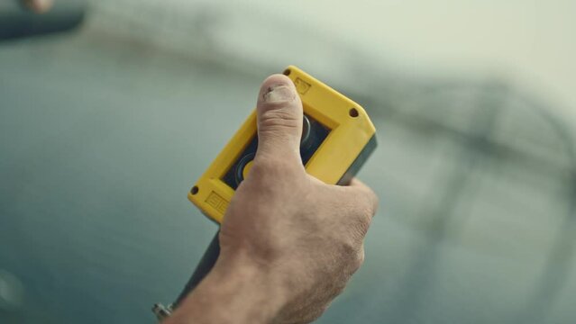 Machine control button.Worker with broken nails holding plastic yellow stop button. Stopping the industrial process. E-stop button in production.