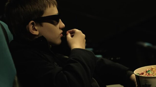 Boy in 3d glasses watches movie and eats popcorn in cinema, slow motion