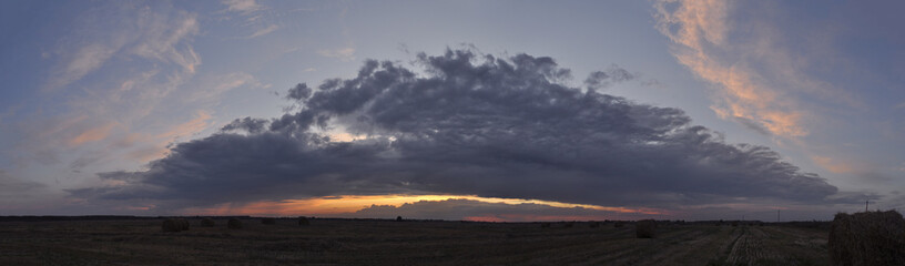 Panorama of a mown field against the background of a menacing sky at sunset