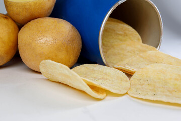 Potato chips spill out of the jar. Next to a can of chips lies potatoes.
