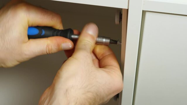 Close-up of a man's hands with a screwdriver screwing a screwdriver into a shelf. Assembling furniture at home with his own hands