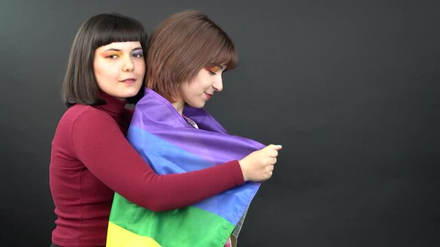 Photo of charming lesbians couple young ladies lovers celebrate parade show support express tolerance all marriages raise gay flag wear isolated black color background 