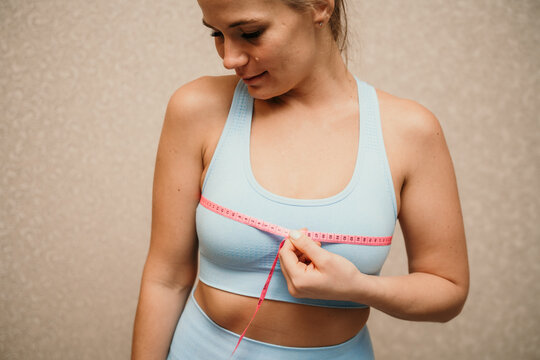 Cropped view of slim woman measuring breasts with tape measure at home, close up. A European woman checks the result of a weight loss diet or liposuction indoors. Healthy lifestyle.