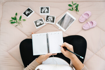 A Pregnancy dairy.Top view of pregnant woman writing thoughts down in notebook for memory,x-ray image of her baby and shoes.Concept of pregnancy, Maternity prenatal care.