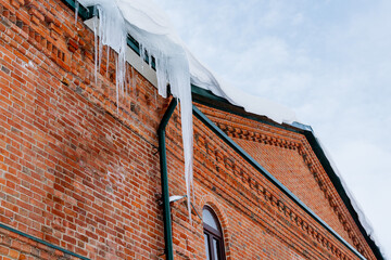 A huge icicle hangs from the roof of a brick building. Dangerous and sharp icicles on the facade of the house. Be careful in winter.natural phenomena.