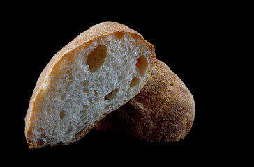 Ciabatta, a loaf of bread cut in half isolated on a black background.