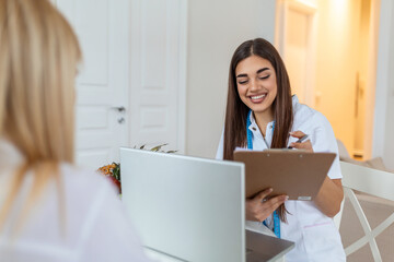 Doctor nutritionist, dietician and female patient on consultation in the office. young smiling female nutritionist in the consultation room. Nutritionist desk with healthy fruit and measuring tape.