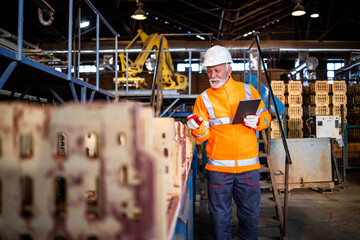 Industrial worker with radio communication and tablet computer walking through the industry manufacturing factory and checking products.