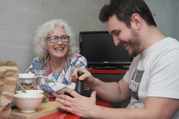 Mother and adult son laughing together in the kitchen while cooking.