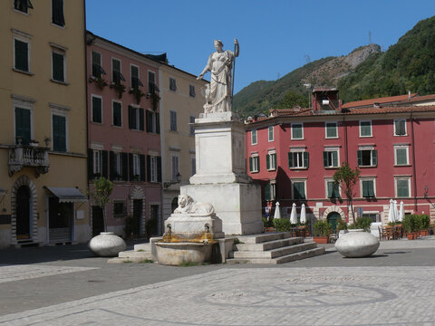 Alberica square in Carrara surrounded by colorful buildings and with the statue dedicated to Beatrice Este made of marble and the lion fountain in the center