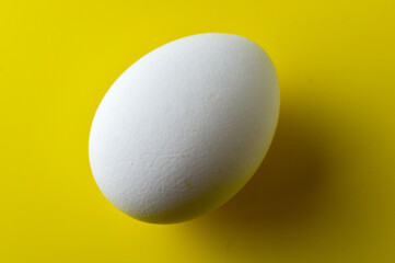 One white chicken egg on a bright yellow background. Close-up