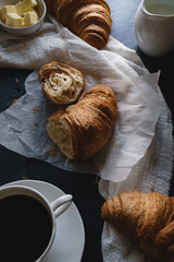 Close up shot of breakfast meal of fresh croissants and coffee. Shot from above, flat lay style. Dark and moody style food image set against a dark background. 