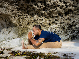 Beach yoga. Asian man practicing Paschimottanasana, Seated Forward Bend Pose. Hands in namaste mudra. Flexible body. Stretching exercise. Healthy spine. Yoga retreat in Bali. Thomas beach