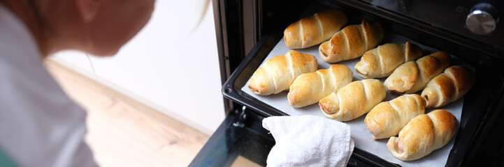 Woman takes out baking sheet of cooked croissants from oven closeup