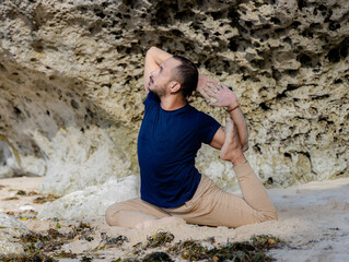 Attractive Asian man practicing Eka Pada Rajakapotasana, One Legged King Pigeon Pose. Chest opener improving breathing. Healthy lifestyle. Flexible body. Yoga retreat. Thomas beach, Bali