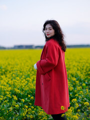 An Asian woman in a red trench coat stands in a field of rape flowers