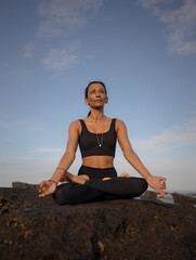 Fototapeta na wymiar Meditation and yoga on the beach. Asian woman sitting on the rock in Lotus pose. Padmasana. Hands in gyan mudra. Yoga retreat. Healthy lifestyle. Copy space. Mengening beach, Bali