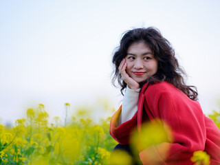 Naklejka na ściany i meble An Asian woman in a red trench coat stands in a field of rape flowers