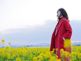 An Asian woman in a red trench coat stands in a field of rape flowers